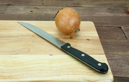 Onion on a wooden chopping board with knifeの写真素材