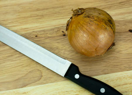 Onion on a wooden chopping board with knifeの写真素材