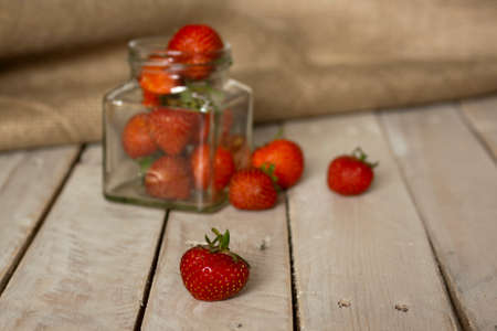 Fresh stawberries spilt on wooden table from jarの写真素材
