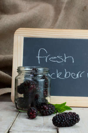 Fresh blackberries spilt on wooden table from jarの写真素材