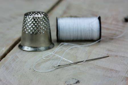 Needle cotton and thimble used for sewing left on a wooden surfaceの写真素材
