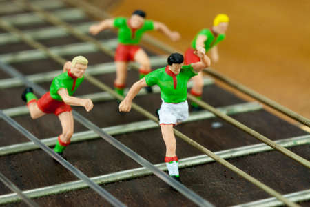 Miniature men in a race running down the arm of a guitar.の写真素材