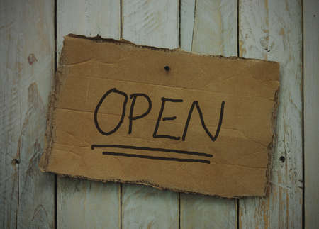 Cardboard sign on a wooden background saying open. Vintage filter applied.の写真素材