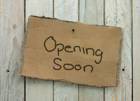 Cardboard sign on a wooden background saying opening soonの写真素材