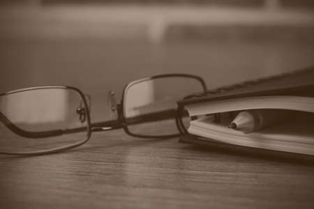 Black spiral bound notebook with pen on wooden background. Black and white filter applied.の写真素材