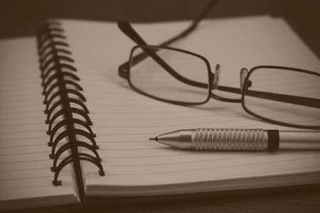 Black spiral bound notebook with pen on wooden background. Black and white filter applied.