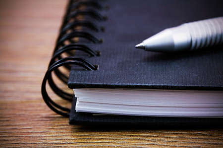 Black spiral bound notebook with pen on wooden background. Retro filter applied.
