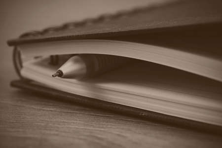 Black spiral bound notebook with pen on wooden background. Black and white filter applied.