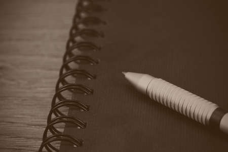 Black spiral bound notebook with pen on wooden background. Black and white filter applied.