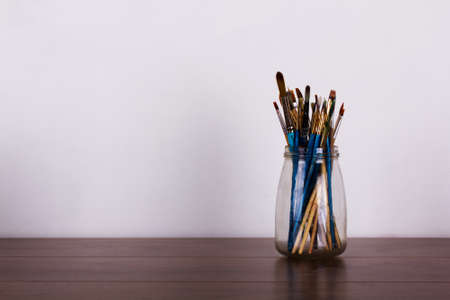 Paint brushes in a glass pot against a white background
