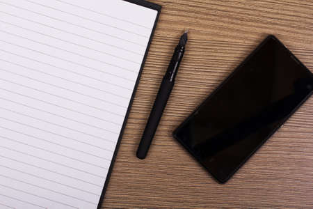 Lay flat image of an open notebook and phone on a wooden surface