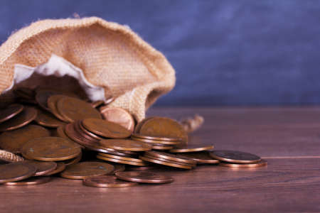 Bag of old coins spilt over a wooden surface