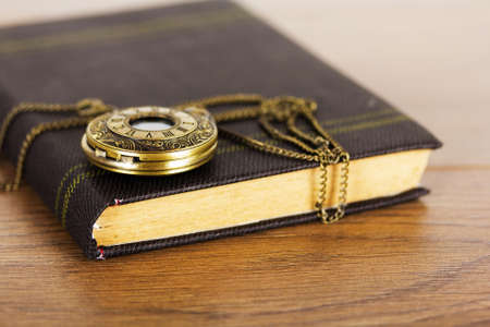 Pocket watch and book against a rustic wooden backgroundの写真素材