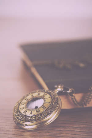 Pocket watch and book against a rustic wooden background Vintage Retro Filter.