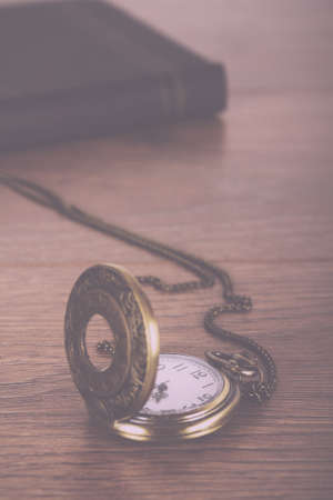 Pocket watch and book against a rustic wooden background Vintage Retro Filter.