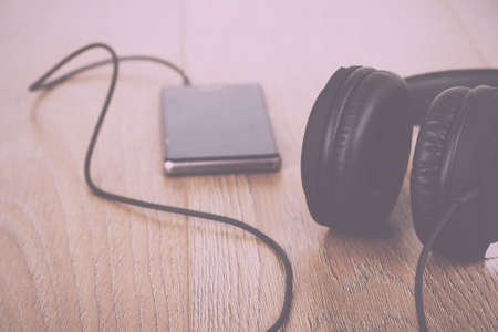 Headphones and mobile phone on a wooden surface Vintage Retro Filter.の写真素材