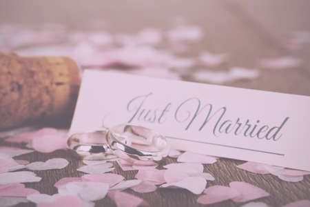 pair of white gold wedding rings on a wooden background with confetti Vintage Retro Filter.の写真素材