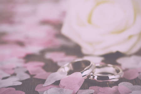 pair of white gold wedding rings on a wooden background with confetti Vintage Retro Filter.の写真素材