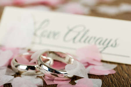 pair of white gold wedding rings on a wooden background with confettiの写真素材