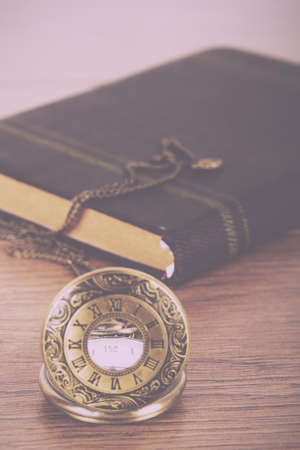 Pocket watch and book against a rustic wooden background Vintage Retro Filter.の写真素材