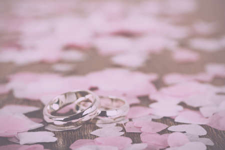 pair of white gold wedding rings on a wooden background with confetti Vintage Retro Filter.の写真素材
