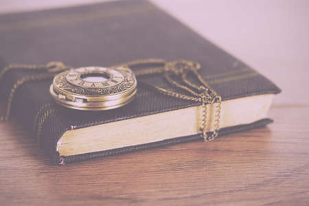 Pocket watch and book against a rustic wooden background Vintage Retro Filter.の写真素材