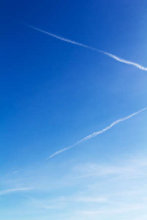 Clear blue sky with light white clouds and trails