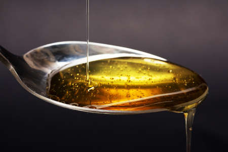 Honey pouring from a spoon against a dark backgroundの写真素材