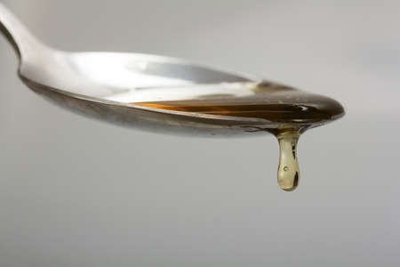Honey pouring from a spoon against a light backgroundの写真素材