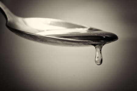 Honey pouring from a spoon against a light backgroundの写真素材