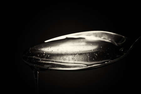 Honey pouring from a spoon against a dark backgroundの写真素材