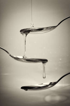 Honey pouring from a spoon against a light backgroundの写真素材