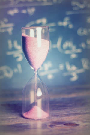 Hourglass against on wooden surface with a blackboard backgroundの写真素材