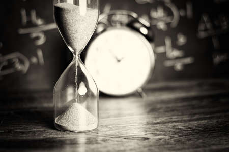 Hourglass against on wooden surface with a blackboard background