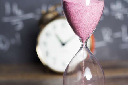 Hourglass against on wooden surface with a blackboard backgroundの写真素材