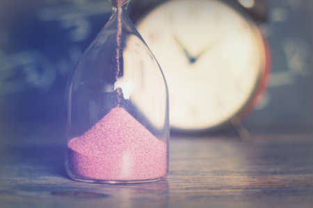 Hourglass against on wooden surface with a blackboard backgroundの写真素材