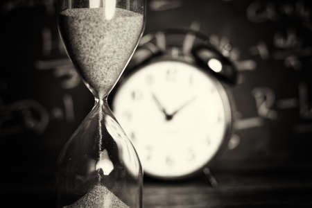 Hourglass against on wooden surface with a blackboard background