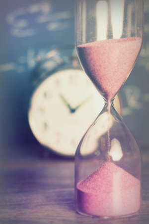 Hourglass against on wooden surface with a blackboard background