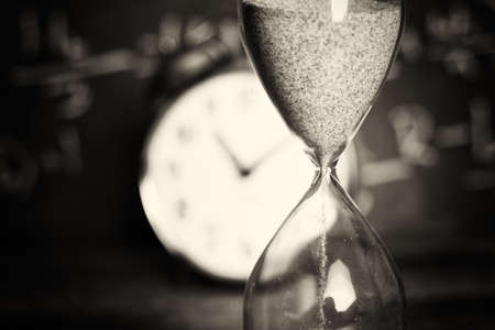 Hourglass against on wooden surface with a blackboard background