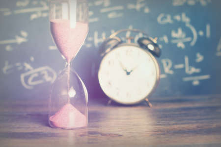 Hourglass against on wooden surface with a blackboard backgroundの写真素材