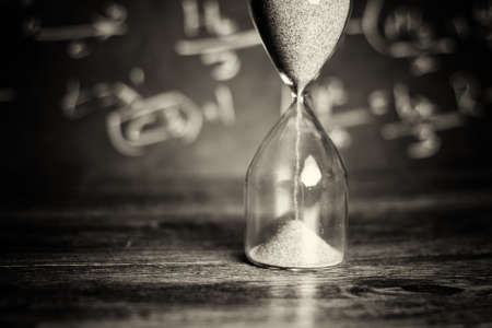Hourglass against on wooden surface with a blackboard backgroundの写真素材