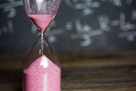 Hourglass against on wooden surface with a blackboard backgroundの写真素材