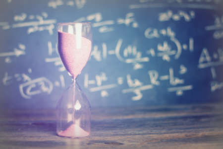 Hourglass against on wooden surface with a blackboard backgroundの写真素材