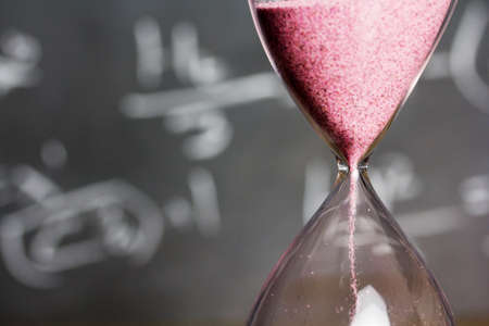 Hourglass against on wooden surface with a blackboard backgroundの写真素材