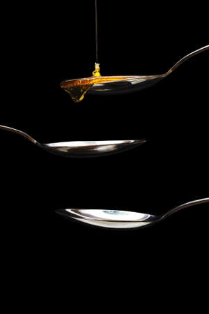 Honey pouring from a spoon against a dark backgroundの写真素材