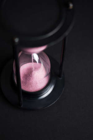Large hourglass with pink sand against a black backgroundの写真素材