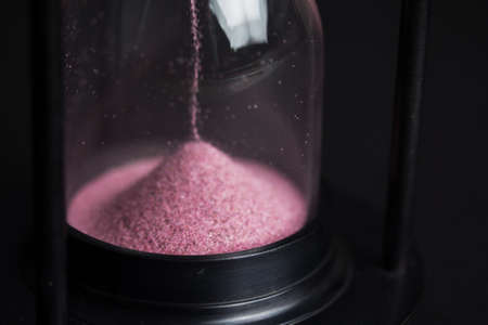 Large hourglass with pink sand against a black backgroundの写真素材