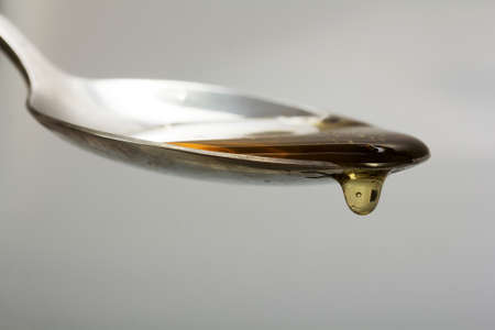 Honey pouring from a spoon against a light backgroundの写真素材