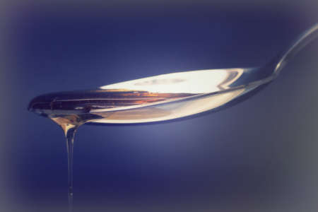 Honey pouring from a spoon against a dark backgroundの写真素材