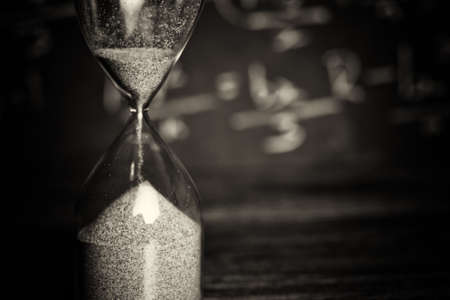 Hourglass against on wooden surface with a blackboard background